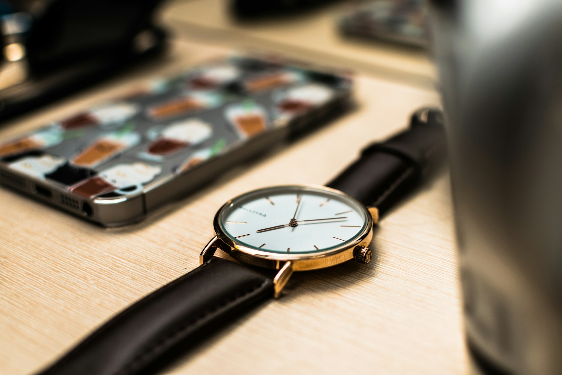 round white and gold-colored analog watch with black leather band on wooden surface